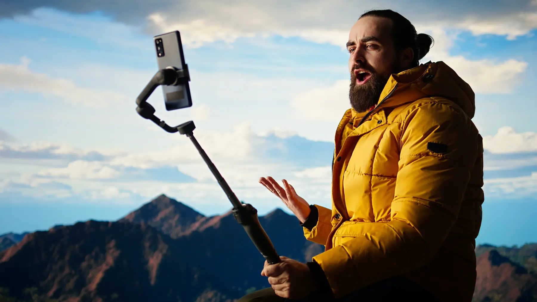 A hiker filming himself on a phone gimbal with mountains behind